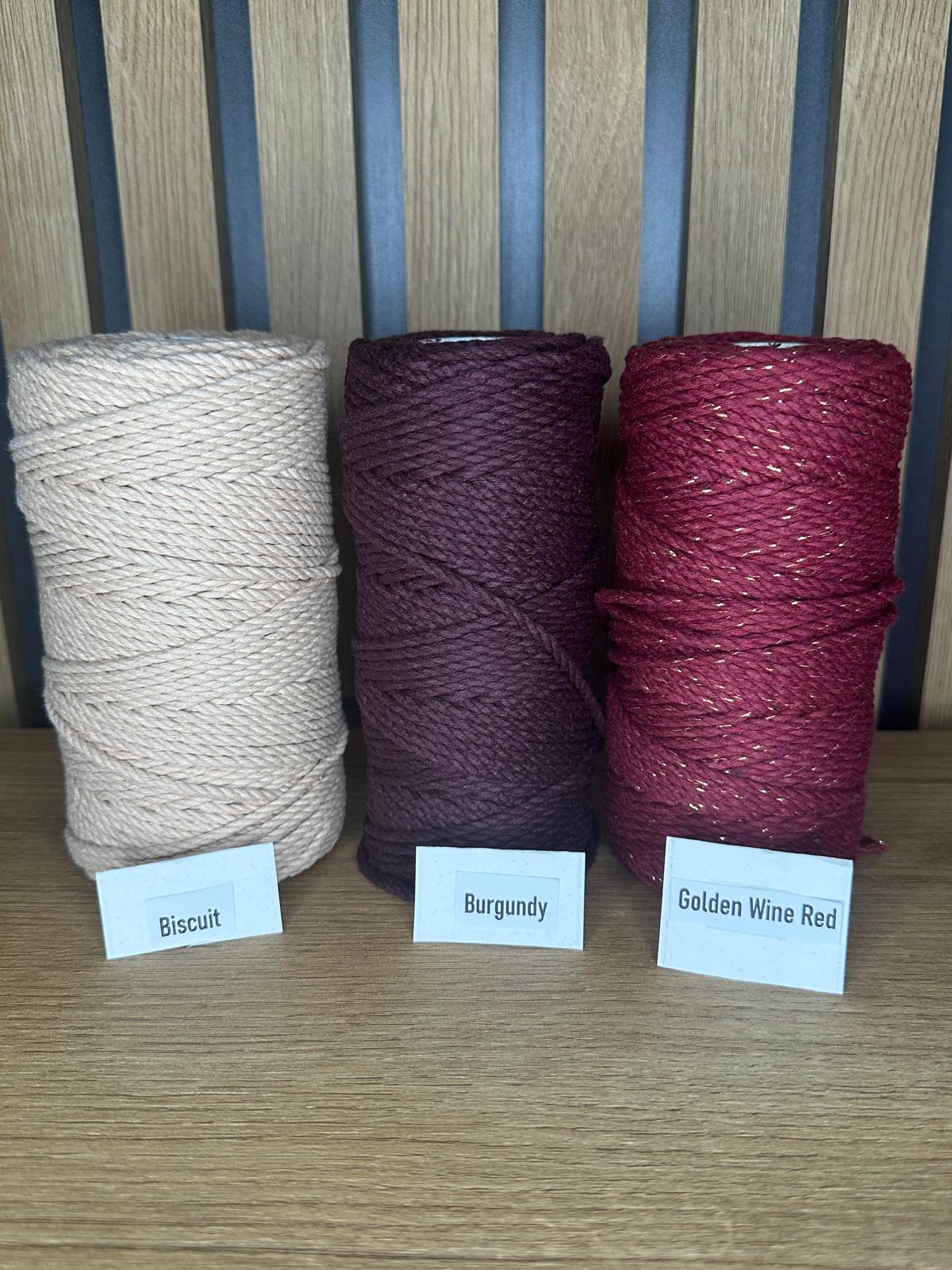 Drei Garnrollen aus Baumwollkordel in den Farben Biscuit, Burgundy und Golden Wine Red, nebeneinander aufgestellt auf Holztisch vor Holzrückwand, mit kleinen Farbschildern.
Herzberg Crafts