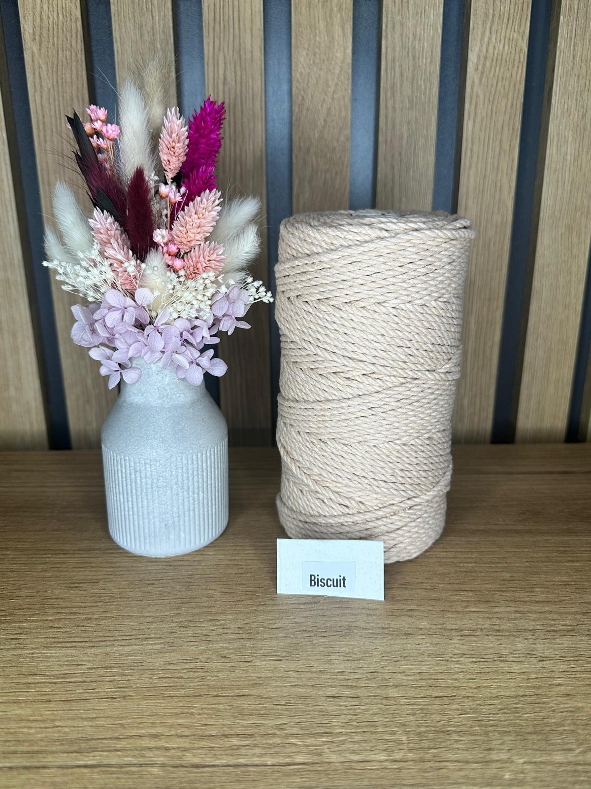 Garnrolle aus gedrehter Baumwollkordel in der Farbe Biscuit, neben einer dekorativen Vase mit Trockenblumen, auf einem Holztisch vor Holzrückwand.
Herzberg Crafts