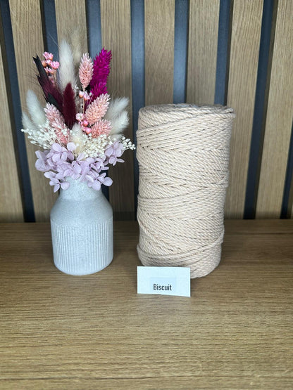 Garnrolle aus gedrehter Baumwollkordel in der Farbe Biscuit, neben einer dekorativen Vase mit Trockenblumen, auf einem Holztisch vor Holzrückwand.
Herzberg Crafts