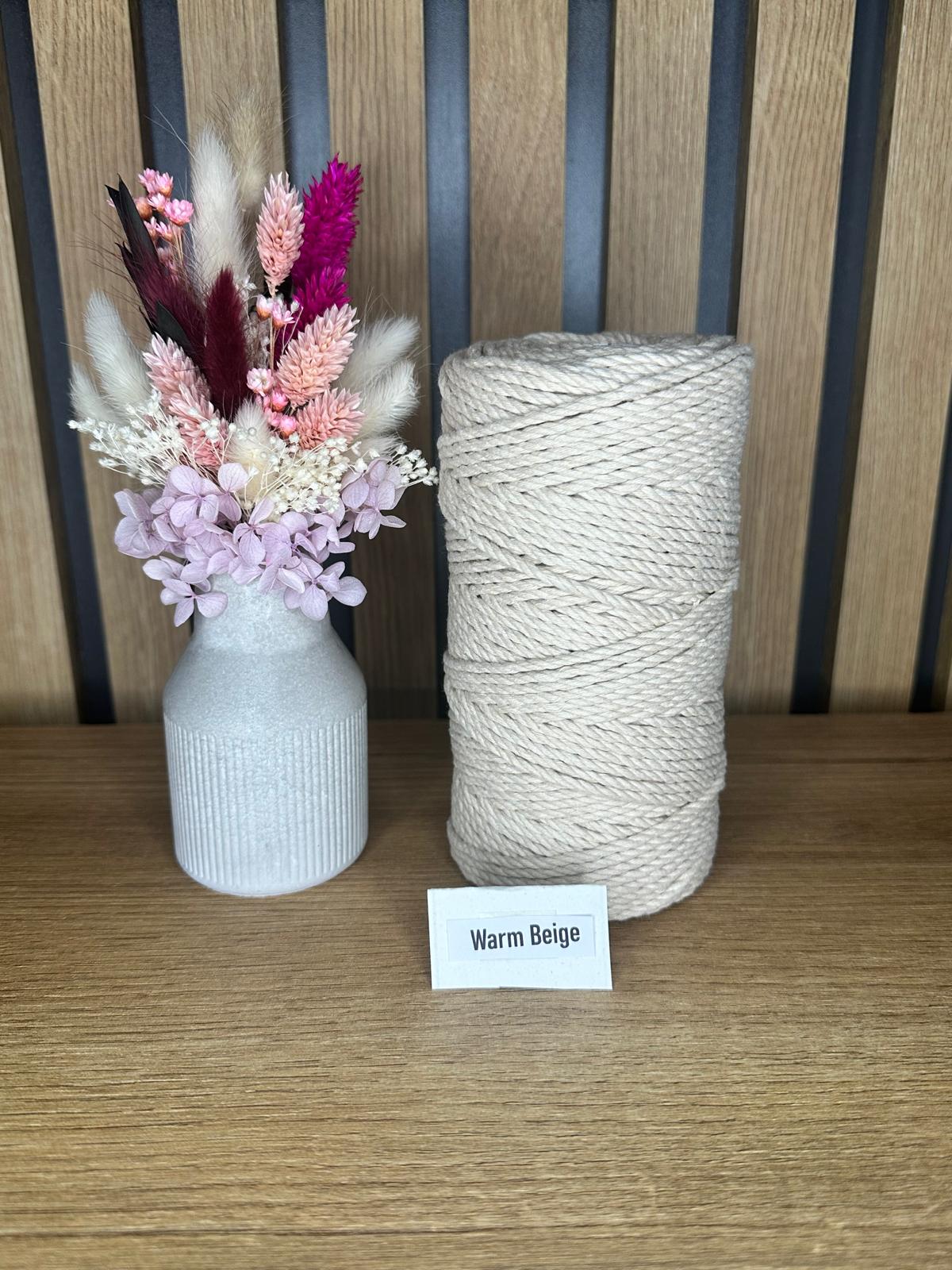 Baumwollgarnrolle in der Farbe Warm Beige, aufrecht stehend neben einer dekorativen Vase mit Trockenblumen, vor einer vertikalen Holzrückwand.
Herzberg Crafts