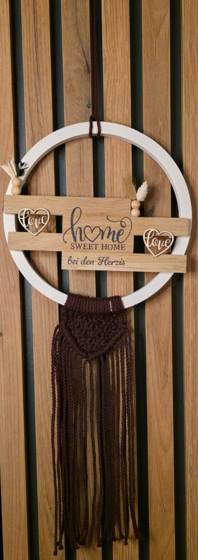 Rundes Türschild mit weißem Keracraftring, Holzklötzchen und Makramee-Fransen in Burgundy, mit der Vinyl-Aufschrift ‚home sweet home bei den Herzis‘, dekoriert mit Holzherzen und Trockenblumen, angebracht an einer vertikalen Holz-Schrankwand.
Herzberg Crafts